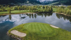 A golf course with a pond in the foreground, a person playing golf, and mountains in the background.