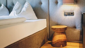 A bedroom with a tufted headboard, a bedside table with a wooden base, a wall-mounted light fixture, and a bedside console.