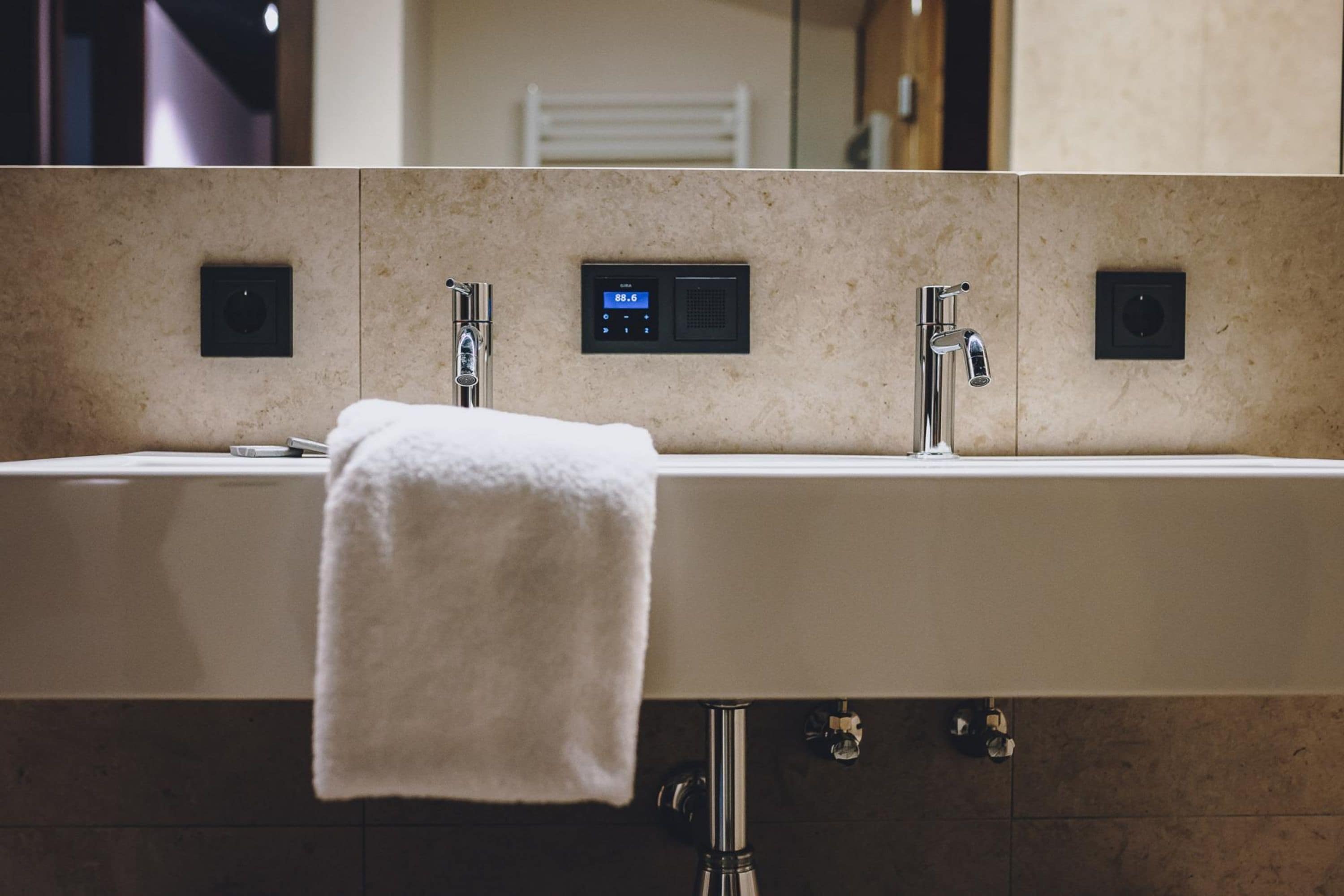 A bathroom with a large sink, a towel hanging on the wall, and a digital display above the sink.