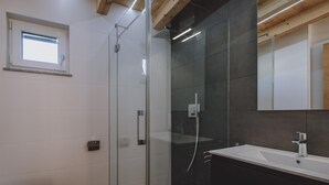 A modern bathroom with a glass shower enclosure, a toilet, and a sink with a mirror above. - FP Appartements - Penthouse (Kaprun)