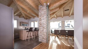 Una cocina moderna con un pilar de piedra, vigas de techo de madera y un comedor con sillas y una mesa.