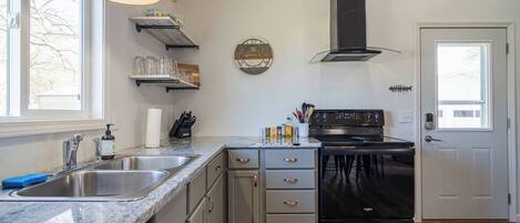 A kitchen with a stainless steel sink, a black stove, and a wooden ceiling.