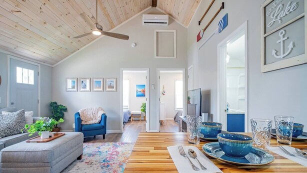 A spacious living room with a high ceiling, a dining area with blue glassware, and a cozy blue armchair. - Walk to Lake Erie — Renovated 2BR Huron Home Near Cedar Point & Kalahari (Huron)