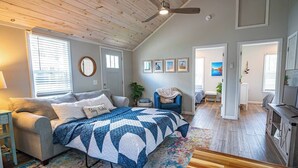 A bedroom with a bed, a blue armchair, a wooden ceiling fan, and a large window with blinds. - Walk to Lake Erie — Renovated 2BR Huron Home Near Cedar Point & Kalahari (Huron)