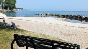 A beach with a bench and lounge chairs, a rocky breakwater, and calm water. - Walk to Lake Erie — Renovated 2BR Huron Home Near Cedar Point & Kalahari (Huron)