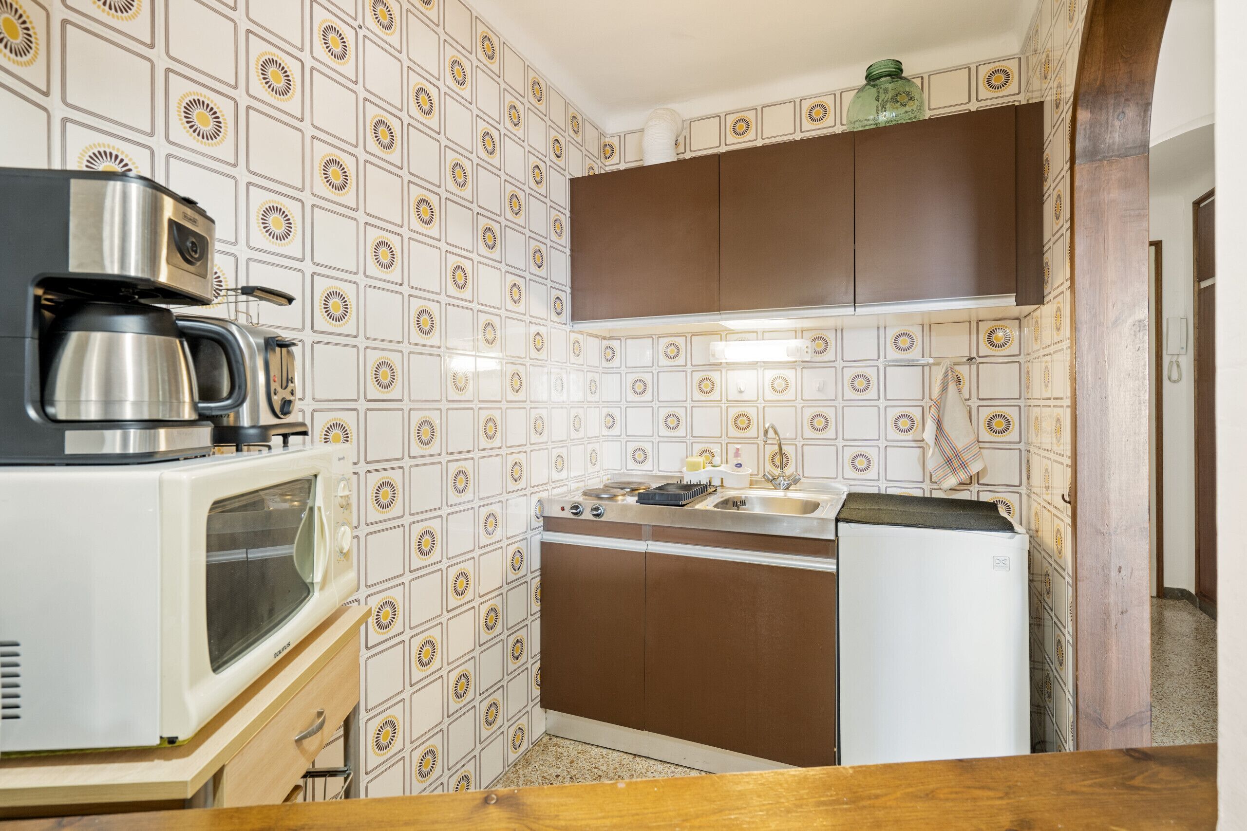 Una cucina compatta con macchina da caffè, forno a microonde e lavandino.