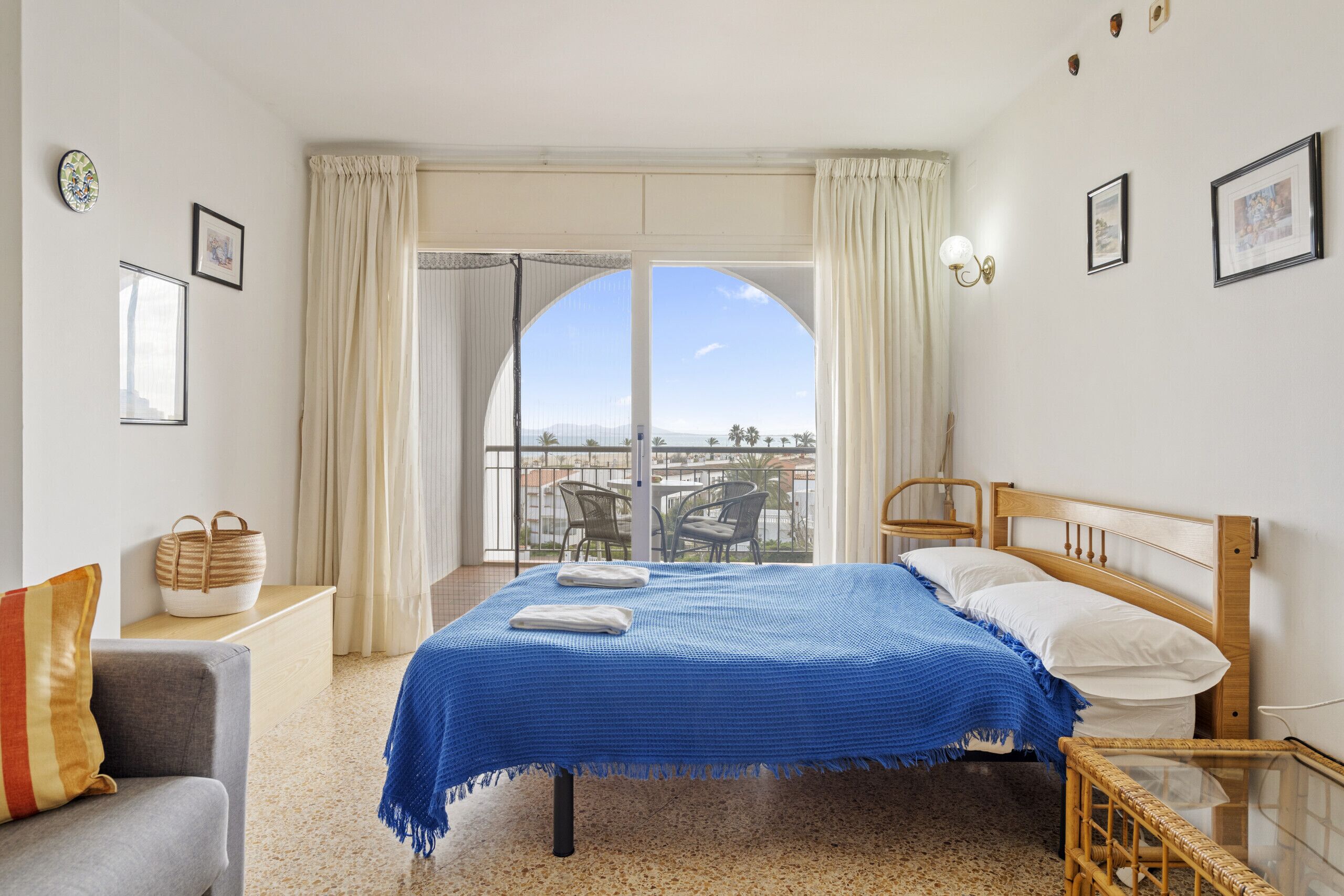 Une chambre d’hôtel avec un lit, un canapé, un fauteuil en osier, une table en verre et un balcon avec vue.