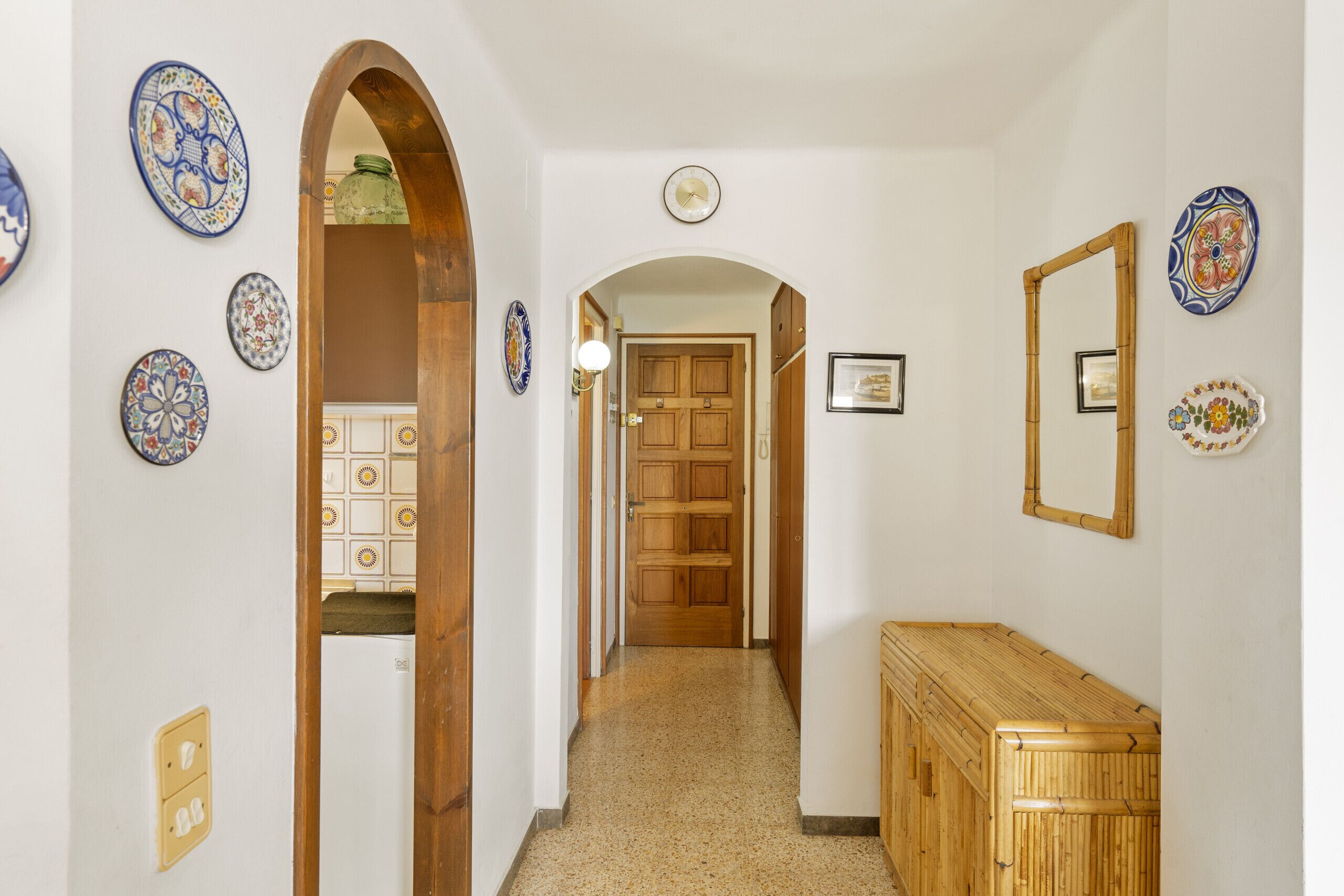 Un couloir avec un banc en bois, une porte au fond et des assiettes décoratives accrochées aux murs.