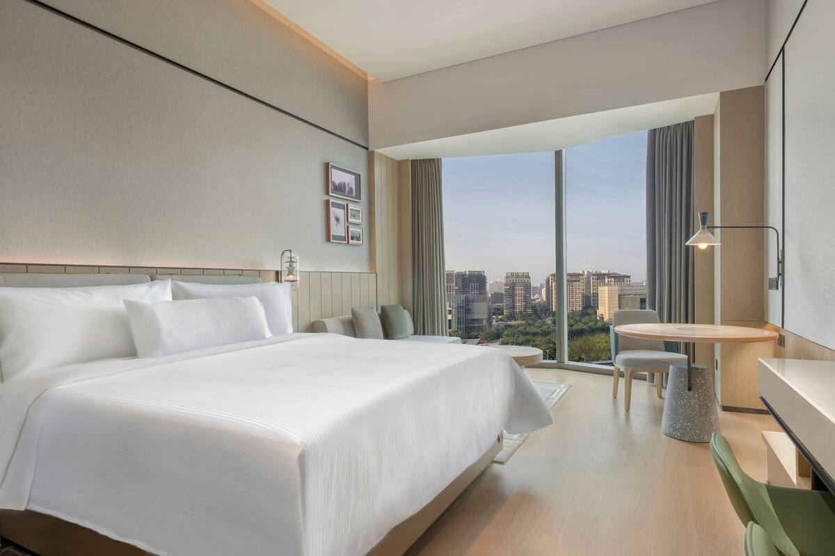 Ett modernt hotellrum med en stor säng, ett skrivbord och utsikt över stadsbilden.