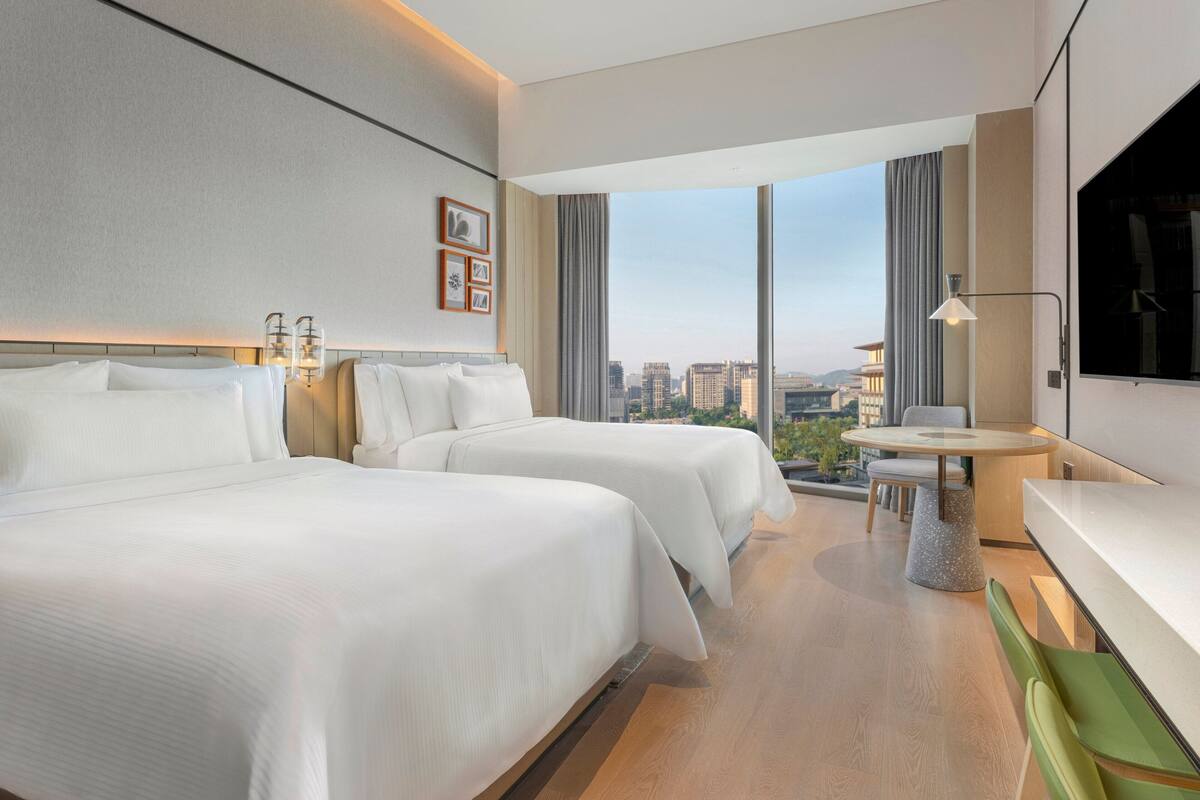 Ett hotellrum med två sängar, ett skrivbord och ett stort fönster med utsikt över staden.