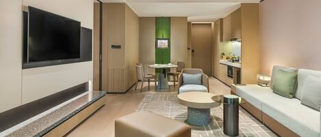 Una habitación de hotel moderna con televisión de pantalla plana, un sofá, una mesa de comedor y una pequeña cocina.