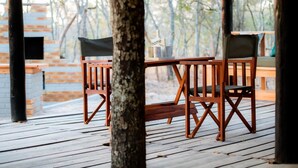 A wooden deck with a table and chairs, a sign reading "home family", and a brick wall in the background. - Rustic Luxury Farm Cabin Located in Hwedza - 2031 (Wedza)