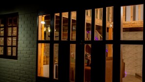 A dark wooden door with multiple windows, revealing an interior with a brick wall and a staircase. - Rustic Luxury Farm Cabin Located in Hwedza - 2031 (Wedza)