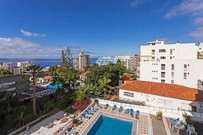 A hotel with a rooftop pool, surrounded by palm trees and buildings.