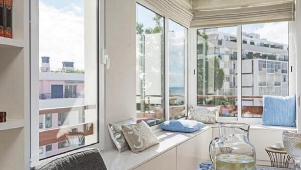 Un balcone con angolo salotto, ampie finestre e vista su edifici e mare.