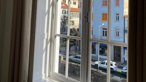 Ein Zimmer mit einem großen Fenster und Blick auf Gebäude und geparkte Autos vor dem Haus.