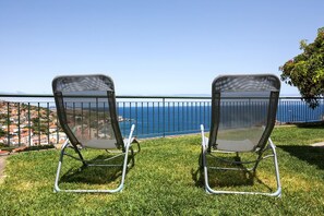 Zwei Netzstühle auf einer grünen Rasenfläche mit Blick auf das Meer und eine Küstenstadt.