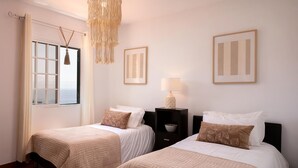 A hotel room with two beds, a chandelier, a window with curtains, and framed artwork on the walls. - Sea View Villa by Homie (Santa Cruz)