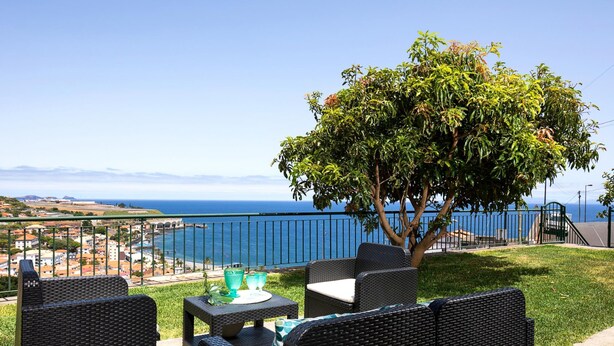 An outdoor seating area with wicker furniture, a table with a green placemat, and a view of the sea and distant buildings. - Sea View Villa by Homie (Santa Cruz)