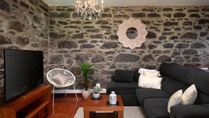 A living room with a stone wall, a flat-screen TV, a white chair, a black sofa, and a wooden coffee table. - Sea View Villa by Homie (Santa Cruz)