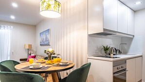 A modern kitchen with white cabinets, a built-in oven, and a dining area with a round table and green chairs. - Urban Paradise I by Homie (Funchal)