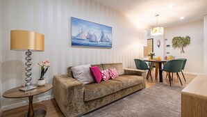 A living room with a sofa, a lamp, a painting, and a dining area with chairs and a table. - Urban Paradise I by Homie (Funchal)