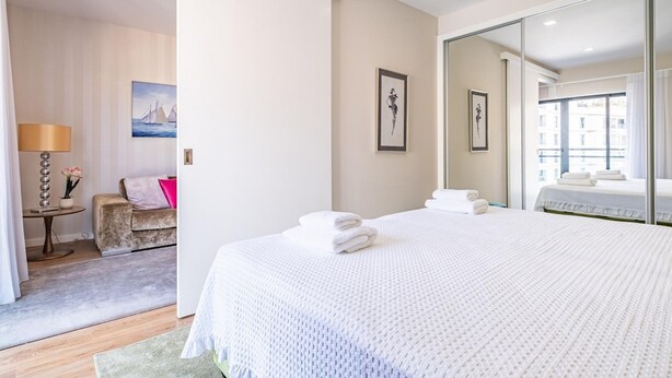 A hotel room with a large bed, a sitting area with a sofa and a table, and a large mirror reflecting the room. - Urban Paradise I by Homie (Funchal)