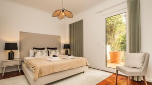 Un dormitorio moderno con una cama grande, dos mesitas de noche, una silla y vistas al verdor por la ventana.