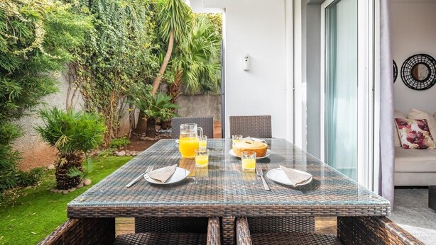 An outdoor dining area with a glass table, wicker chairs, and a view of a lush garden. - Home to Stay by Homie (Funchal)