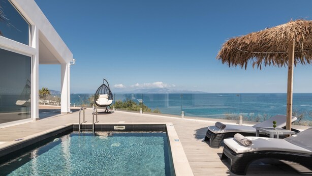 A poolside area with a clear view of the ocean, a thatched umbrella, and lounge chairs. - Luxury Villa Cavo Mare Meltemi With Private Pool Jacuzzi (Zakynthos)