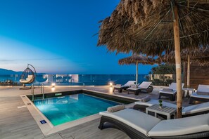 Ein Poolbereich mit Liegestühlen, einem Whirlpool und Blick auf das Meer im Abendlicht.