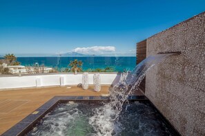 A rooftop pool with a waterfall feature, overlooking a coastal view.
