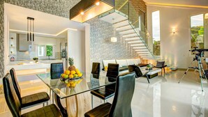 Eine moderne Küche mit Einbauofen, ein Essbereich mit Glastisch und schwarzen Stühlen sowie eine Treppe mit Glasgeländern.
