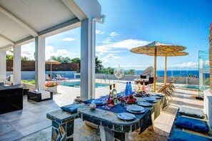 A rooftop terrace with a dining table set for six, overlooking a pool and the ocean.