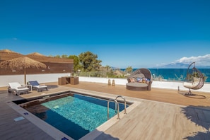 A rooftop pool area with lounge chairs, a hanging chair, and a view of the sea.
