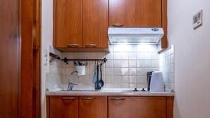 A kitchen with wooden cabinets, a white countertop, a built-in oven, and a wall-mounted exhaust hood. - Katrina Studio 2 Ground Floor (Rethymno)
