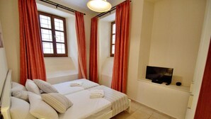 A bedroom with a bed, pillows, a TV, and red curtains. - Katrina Studio 2 Ground Floor (Rethymno)