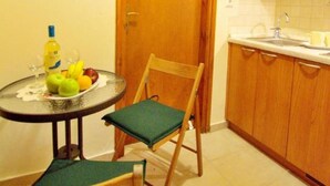 A compact kitchen with wooden cabinets, a small dining table with chairs, and a fruit bowl. - Katrina Studio 2 Ground Floor (Rethymno)