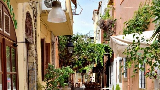 A narrow street with buildings on either side, outdoor seating, and potted plants. - Katrina Studio 2 Ground Floor (Rethymno)