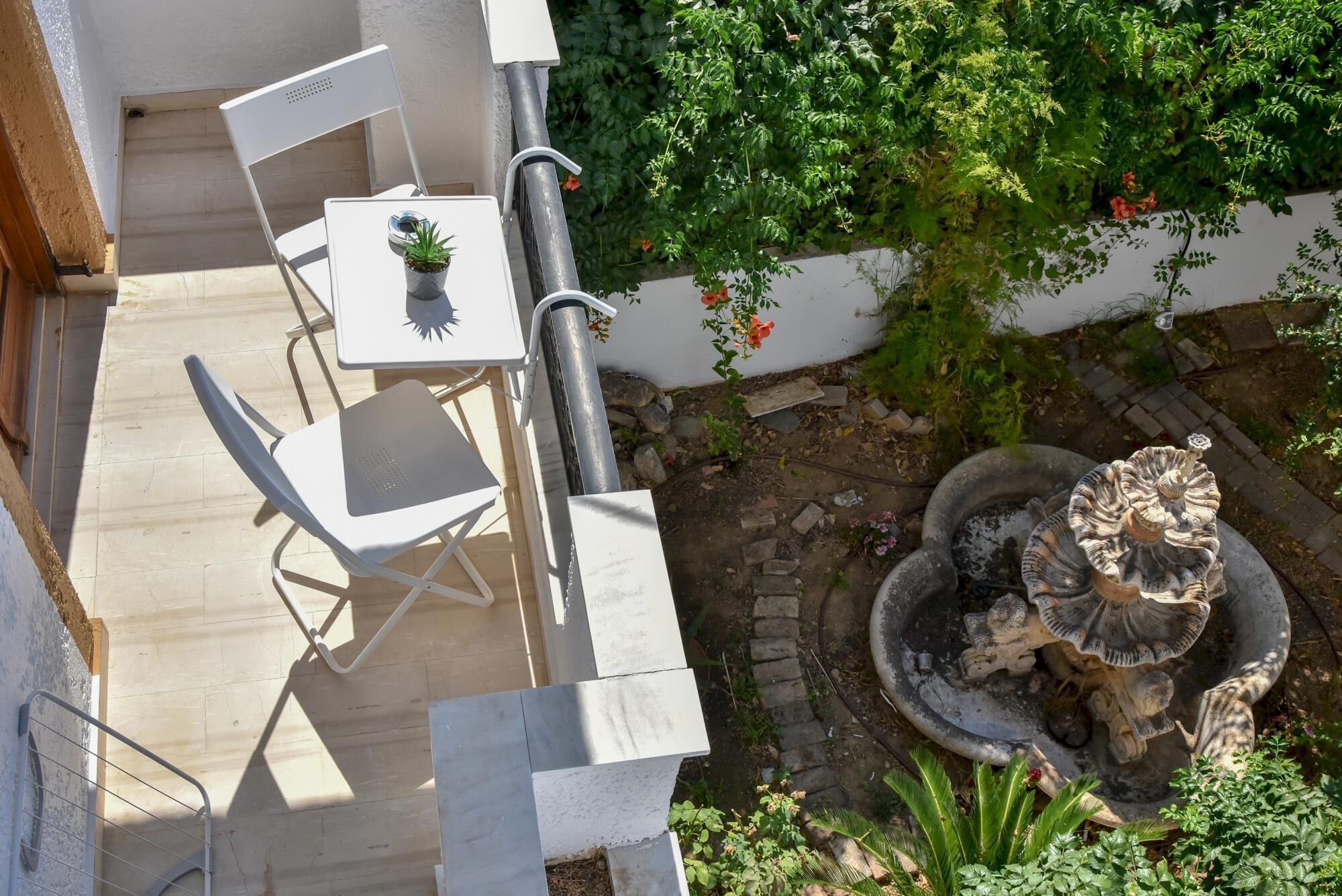 Un patio con mesa y sillas, un pequeño jardín con una fuente y una pared cubierta de plantas trepadoras.