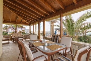 An outdoor patio with a wooden ceiling, a glass-top table, and multiple chairs. - Yialos Ammos Beach Residence by Estia (Hersonissos)