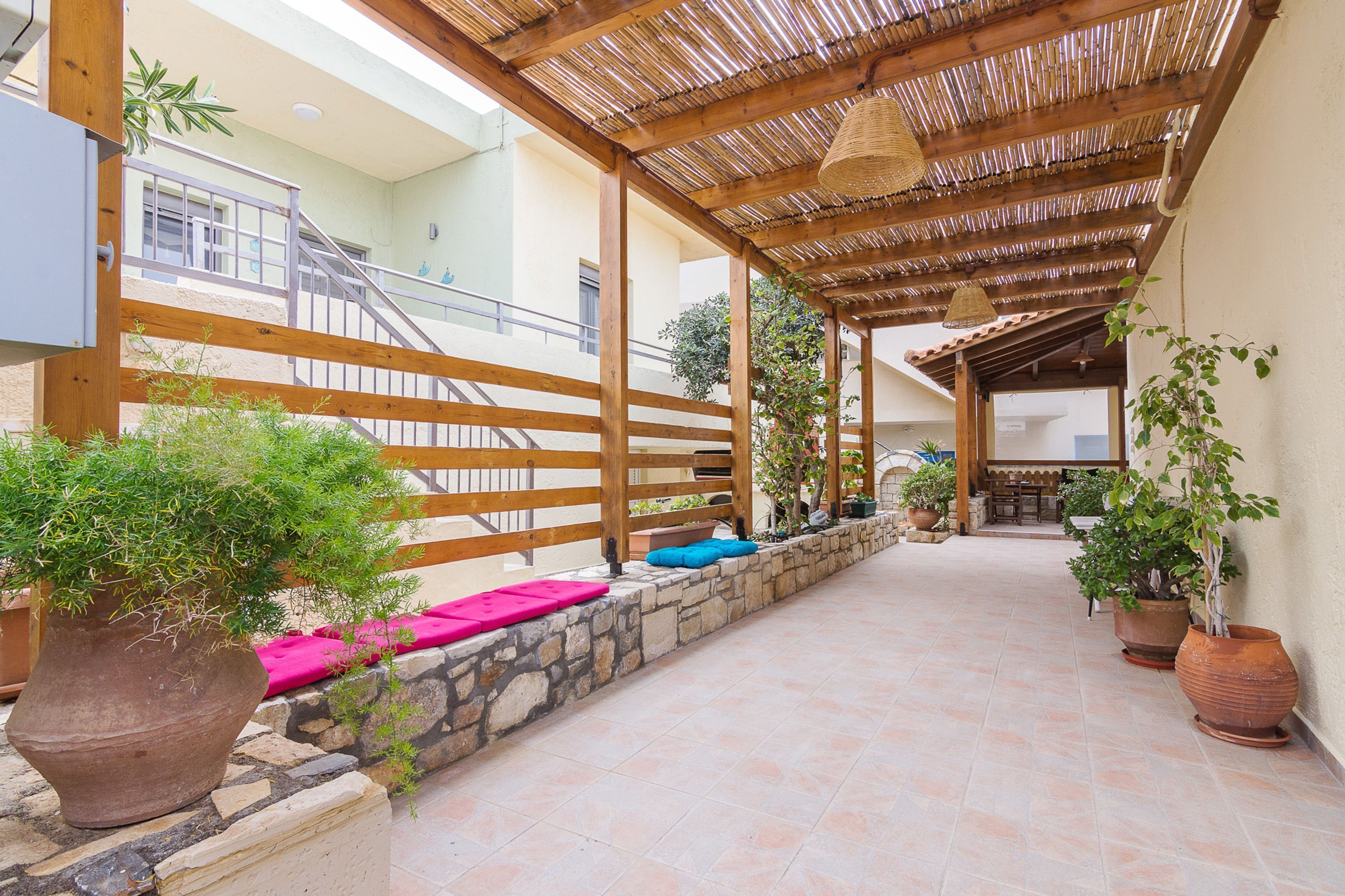 A covered outdoor area with a wooden pergola, stone walls, and potted plants.