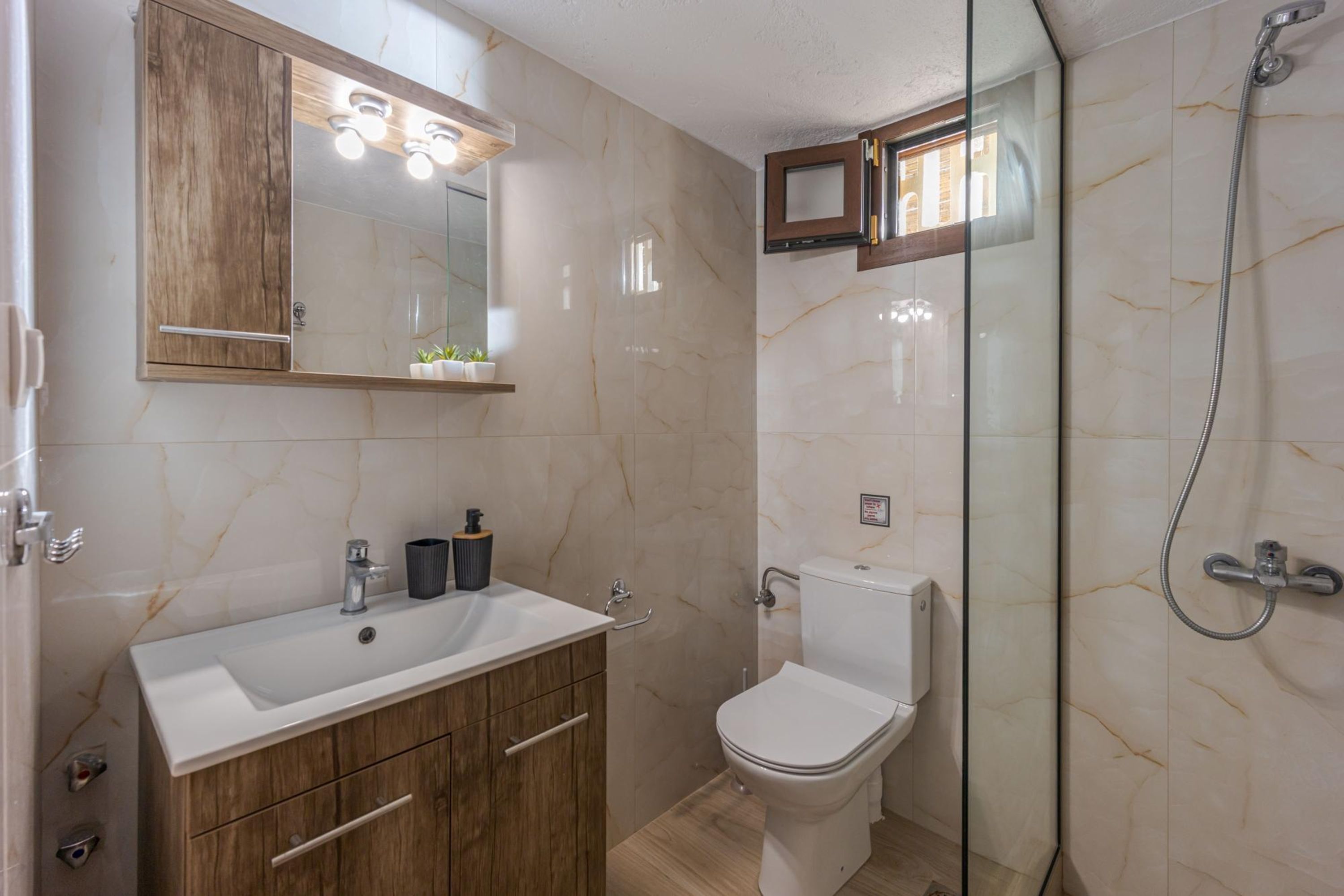 Een badkamer met een houten wastafelmeubel, een witte wasbak, een toilet en een douchecabine met glazen wanden.