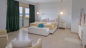 Quarto de hotel moderno com uma cama grande, um sofá, uma mesa de cabeceira e vista para o mar.