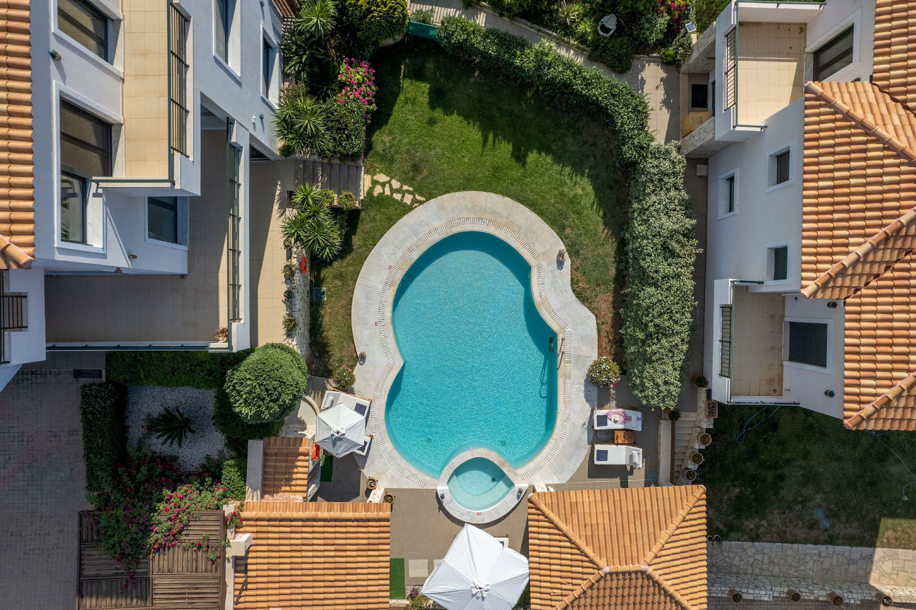 An aerial view of a residential building with a swimming pool surrounded by greenery and a patio area with umbrellas.