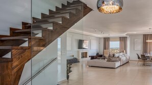 Uma sala de estar moderna com escada de vidro, lareira, sofá e área de refeições.