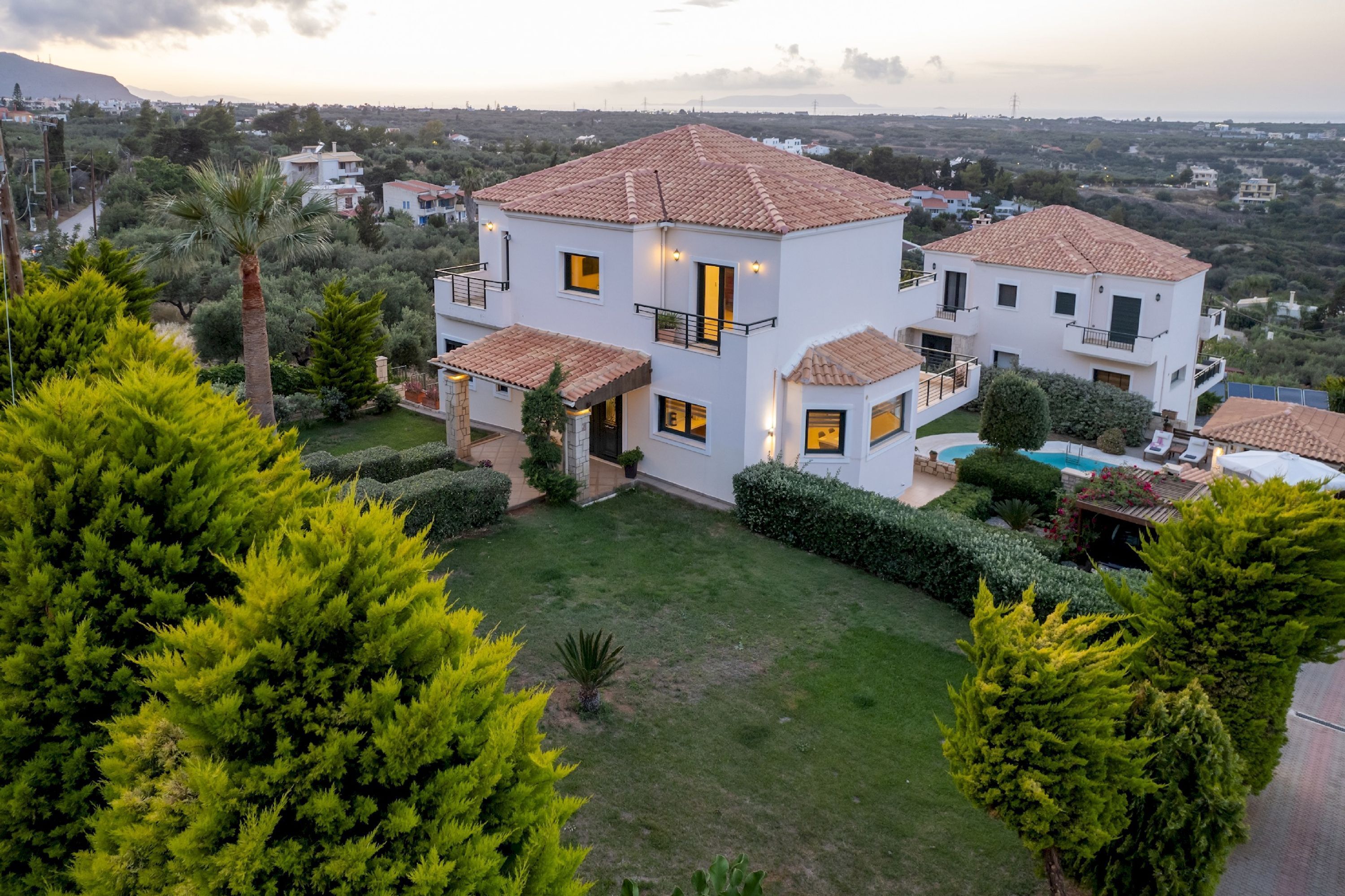 Una moderna casa a due piani con tetto in tegole, circondata da vegetazione rigogliosa e un prato curato.