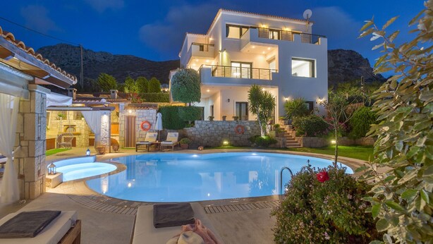 Uma casa moderna de dois andares com piscina, área de estar externa e montanhas ao fundo.
