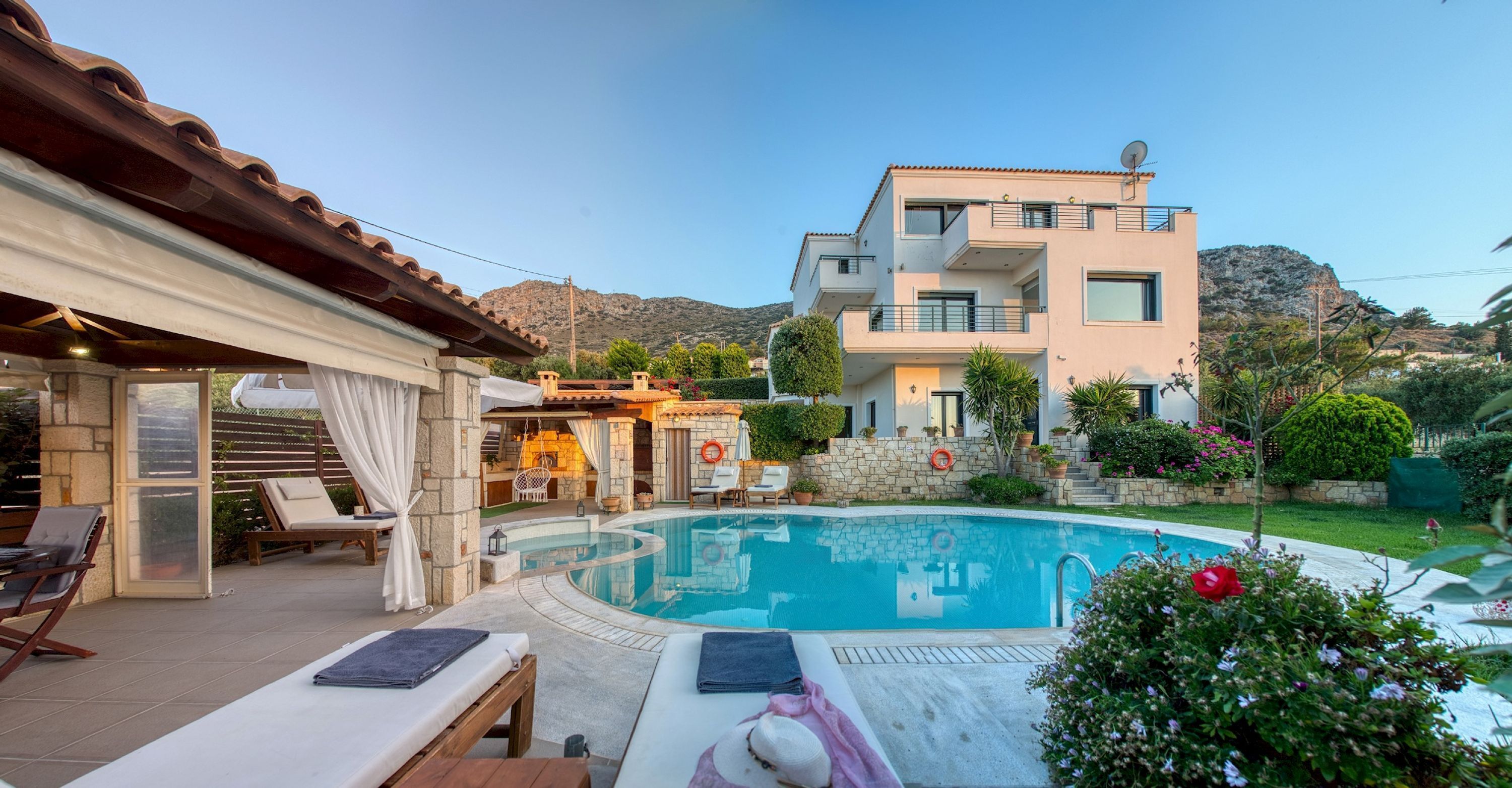 A modern two-story building with a swimming pool, outdoor seating, and a mountainous backdrop.