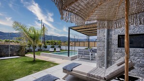 Patio esterno moderno con poltrona da relax, piscina e parete di pietra sullo sfondo.